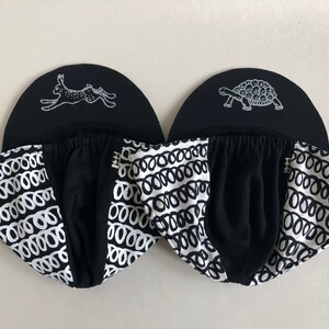 May include: Two black and white patterned baseball caps with a white rabbit and a white turtle graphic on the front of each cap.