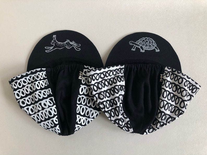 May include: Two black and white patterned baseball caps with a white rabbit and a white turtle graphic on the front of each cap.