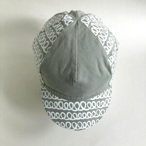 May include: A gray cycling cap with a white patterned design. The pattern is a series of white loops.