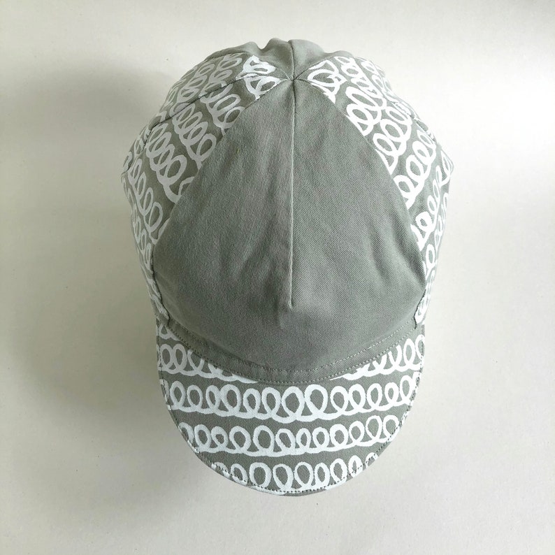 May include: A gray cycling cap with a white patterned design. The pattern is a series of white loops.