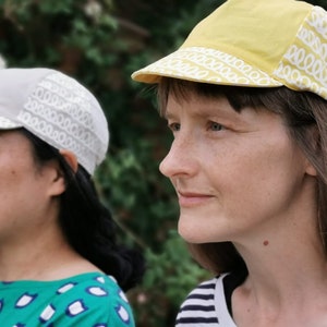 May include: Two people wearing cycling caps with a white patterned design. One cap is yellow and the other is gray.