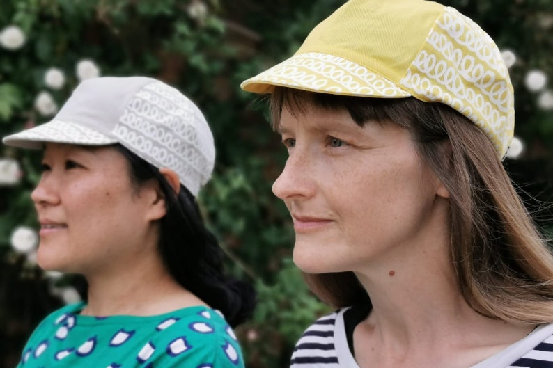May include: Two people wearing cycling caps with a white patterned design. One cap is yellow and the other is gray.