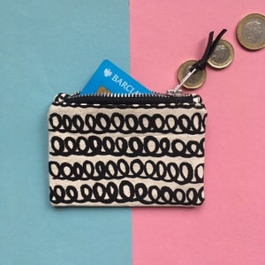 May include: A small black and white zippered pouch with a repeating pattern of black circles. The pouch is open and a blue credit card with the word "BARCLAY" is partially visible inside.