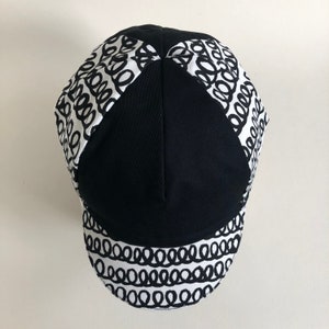May include: A black and white cycling cap with a patterned design of black circles on a white background.