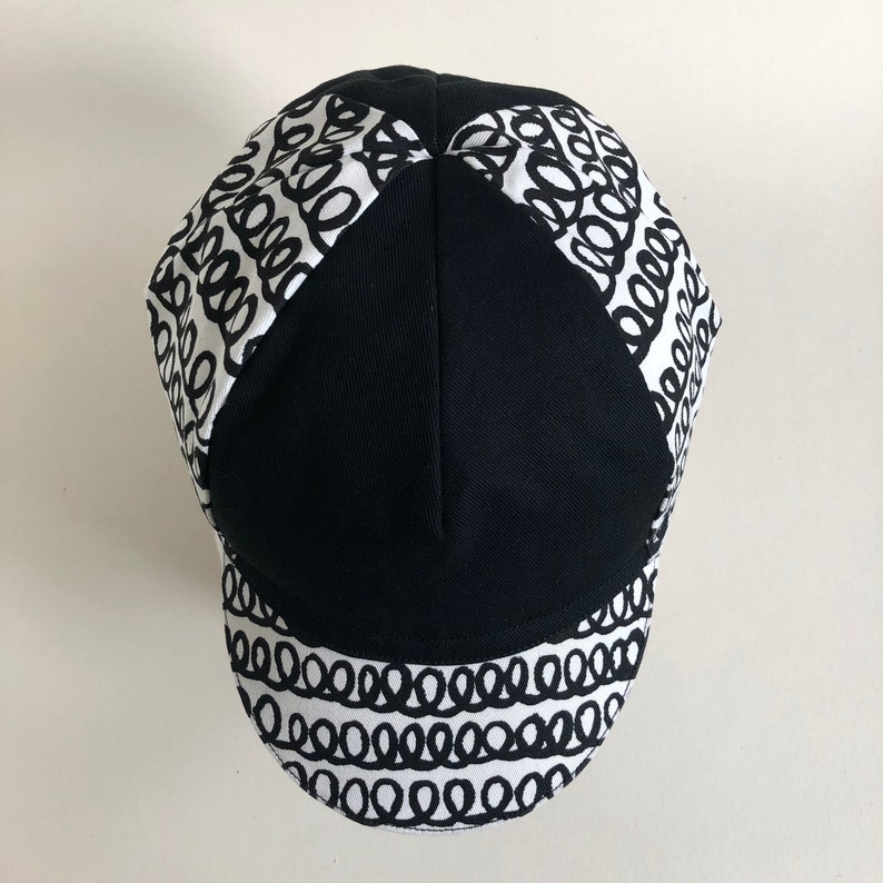 May include: A black and white cycling cap with a patterned design of black circles on a white background.