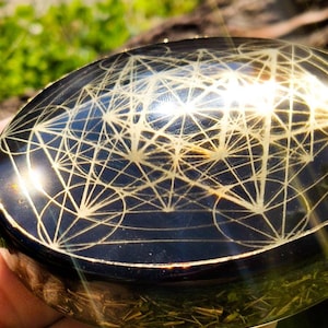 May include: A round, black metal bowl with a gold geometric design. The bowl is slightly curved and has a shiny finish.
