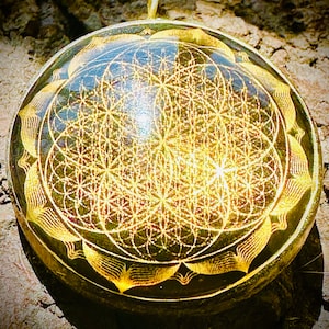 Pode incluir: Um pingente redondo e transparente com um design floral dourado. O pingente tem uma argola dourada na parte superior para pendurar. O design apresenta um padrão geométrico no centro e uma borda floral. O pingente tem aproximadamente 5 cm de diâmetro.