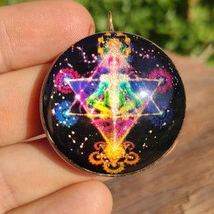 May include: A round, gold-toned pendant featuring a colourful, geometric design on a black background. The design incorporates a star, a diamond shape, and a swirling pattern. The pendant is bordered in black and has a gold loop at the top.