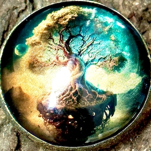 Puede incluir: Un colgante redondo de color dorado con una imagen de resina de un árbol con raíces, rodeado de un cielo azul y verde. El colgante tiene un bucle en la parte superior para colgar.