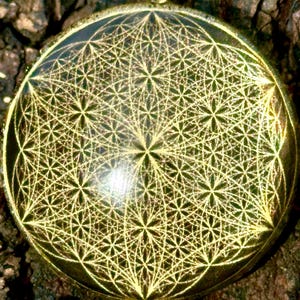 Könnte beinhalten: Ein runder Anhänger mit einem goldfarbenen Metallrahmen und einer dunklen, reflektierenden Oberfläche. Die Oberfläche ist mit einem komplexen, sich wiederholenden geometrischen Muster aus sich überschneidenden Kreisen und Blütenformen graviert.