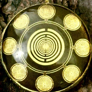 May include: A round pendant featuring a black background with a gold-colored central spiral design surrounded by eight smaller gold-colored circular spiral motifs connected by thin lines, all encased in a metallic frame with a top bail.