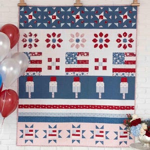 May include: A rectangular quilt featuring a patriotic theme with red, white, and blue fabric patterns. The design includes star motifs, American flag blocks, and popsicle shapes arranged in horizontal rows, finished with a red and white border.