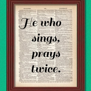 May include: A framed print of a vintage dictionary page with the quote "He who sings, prays twice." in bold black font.