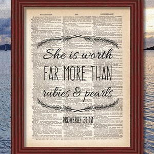 May include: A framed print of a vintage dictionary page with the quote "She is worth far more than rubies & pearls Proverbs 31:10" printed in black ink. The quote is surrounded by decorative floral designs.