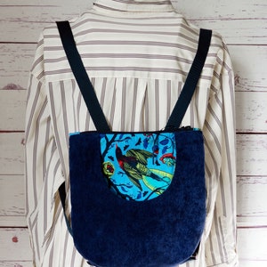May include: A blue corduroy backpack with a blue and green floral print pocket. The backpack has adjustable straps.