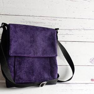 May include: A deep purple corduroy messenger bag featuring a rectangular flap closure, a front pocket, and an adjustable black woven nylon shoulder strap with a silver-toned metal buckle. The bag has a structured shape and a textured fabric surface.