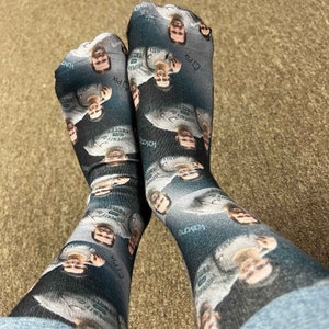 May include: A pair of black and white socks with a repeated pattern of a person's face. The socks have the text "Property of" and "E2 Pix" on them.