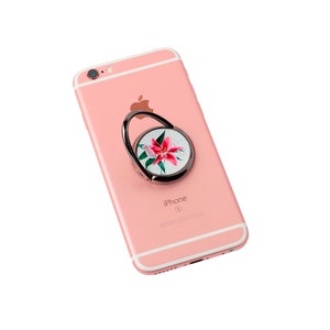 May include: A rose gold phone case with a floral phone ring holder. The ring holder has a white background with a pink lily flower design.