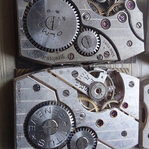 Peut inclure: Gros plan sur des mouvements de montre anciens, avec des engrenages, des bijoux et des inscriptions visibles. Les composants m&eacute;talliques sont agenc&eacute;s avec pr&eacute;cision, montrant la m&eacute;canique interne des montres. Les mouvements de montre sont marqu&eacute;s "SWISS MADE" et "15 JEWELS".