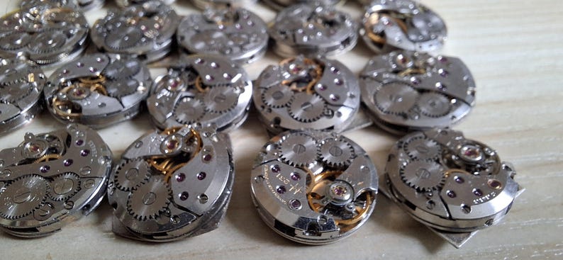 May include: A collection of disassembled watch movements, showcasing intricate gears, springs, and other mechanical components. The silver-toned metal parts are arranged in a grid pattern, with hints of gold and purple accents.