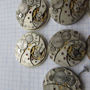 May include: Five antique watch movements with intricate gears and mechanisms. The movements are silver-toned with gold accents and have various markings, including "15 камней" and "2633".