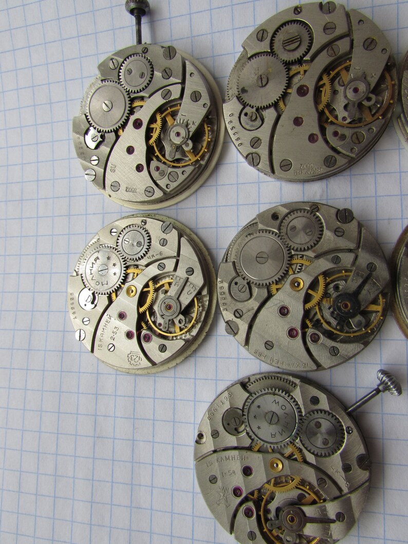 May include: Five antique watch movements with intricate gears and mechanisms. The movements are silver-toned with gold accents and have various markings, including "15 камней" and "2633".