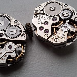Peut inclure: Deux mouvements de montre Bulova vintage, pr&eacute;sentant des engrenages, des bijoux et des composants m&eacute;caniques complexes. Les m&eacute;canismes argent&eacute;s sont marqu&eacute;s "Bulova Watch Co. USA" et "21 Jewels". L'image met en &eacute;vidence la pr&eacute;cision de l'horlogerie.