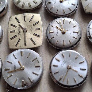 May include: A collection of vintage watch faces with silver and gold tones. The watch faces are round and square, with various styles of hands and hour markers. Some have visible brand names.
