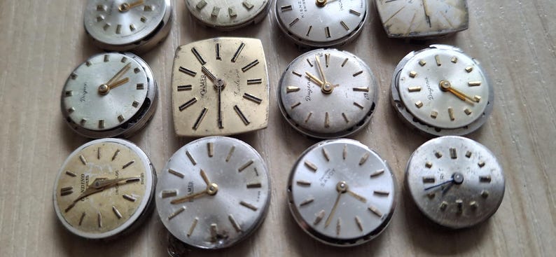 May include: A collection of vintage watch faces with silver and gold tones. The watch faces are round and square, with various styles of hands and hour markers. Some have visible brand names.