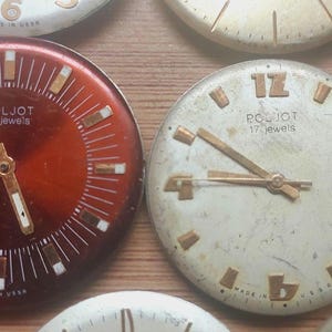 Pode incluir: Uma cole&ccedil;&atilde;o de mostradores de rel&oacute;gios vintage com v&aacute;rios designs e cores. Os mostradores incluem algarismos romanos e ar&aacute;bicos, com ponteiros e marcadores dourados. Alguns mostradores t&ecirc;m a marca "POLJOT" e "17 jewels" impressos.