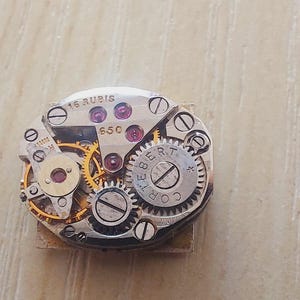 May include: A set of three ceramic mugs with a speckled, matte finish. The mugs are in shades of cream, light gray, and dark gray. Each mug has a simple, minimalist design and a rounded handle. The mugs are likely for coffee or tea.