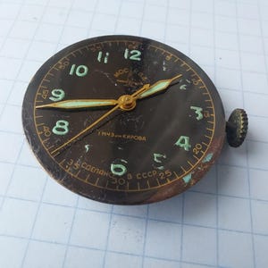 Puede incluir: Esfera de reloj negra vintage con manecillas y n&uacute;meros dorados. La esfera tiene un fondo oscuro con n&uacute;meros y manecillas de color verde claro. La esfera tiene una corona en el lateral y el texto "Made in USSR".