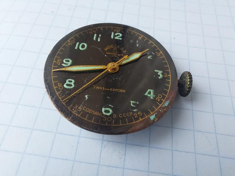 Puede incluir: Esfera de reloj negra vintage con manecillas y n&uacute;meros dorados. La esfera tiene un fondo oscuro con n&uacute;meros y manecillas de color verde claro. La esfera tiene una corona en el lateral y el texto "Made in USSR".