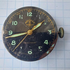Puede incluir: Una esfera de reloj vintage con esfera negra, n&uacute;meros y manecillas verdes. La esfera del reloj tiene un marco dorado y una corona de cuerda en el lateral. El texto "MOCKBA" es visible en la parte superior.