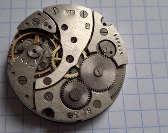 May include: Close-up of a vintage watch movement, showcasing intricate gears, screws, and metal components. The watch mechanism features a complex arrangement of small gears and a balance wheel, with the numbers "3602", "SU", and "465664" visible.