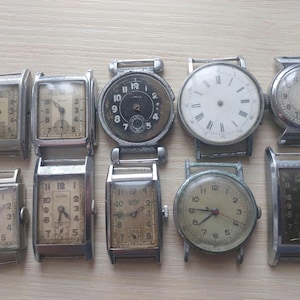 May include: A selection of antique wristwatches, featuring diverse face designs and metal cases. The watches display rectangular and circular faces, with visible numerals and hands. Some have aged dials, indicating their vintage origins.
