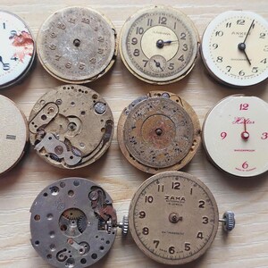 May include: A collection of vintage watch faces and movements, showcasing various designs and mechanical components. The dials feature Roman and Arabic numerals, with hands pointing to different times. Some have visible gears and internal mechanisms.