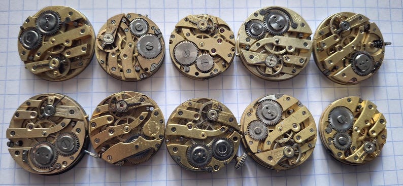 Op de afbeelding: Een verzameling van tien vintage uurwerken, met ingewikkelde messing tandwielen, veren en balanswielen. De cirkelvormige mechanismen zijn in twee rijen gerangschikt en tonen de complexe interne werking van antieke uurwerken.