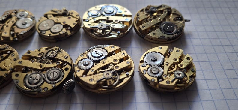 Op de afbeelding: Een verzameling vintage uurwerkonderdelen, met ingewikkelde tandwielen, veren en andere mechanische componenten. De messingkleurige onderdelen zijn gerangschikt op een rasteroppervlak, wat de gedetailleerde vakmanschap benadrukt. Ideaal voor restauratie of knutselprojecten.