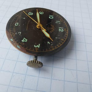 Puede incluir: Una esfera de reloj vintage con esfera marr&oacute;n oscuro, manecillas doradas y n&uacute;meros verdes. La esfera del reloj tiene una peque&ntilde;a corona y est&aacute; marcada con el texto "CCCP". La esfera del reloj tiene aproximadamente 3,8 cm de di&aacute;metro.