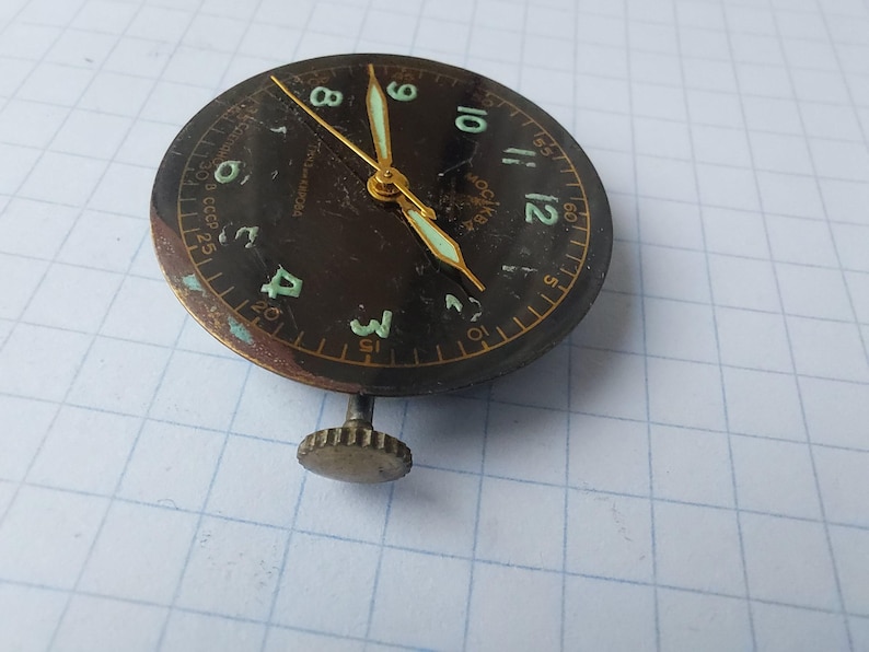 Puede incluir: Una esfera de reloj vintage con esfera marr&oacute;n oscuro, manecillas doradas y n&uacute;meros verdes. La esfera del reloj tiene una peque&ntilde;a corona y est&aacute; marcada con el texto "CCCP". La esfera del reloj tiene aproximadamente 3,8 cm de di&aacute;metro.