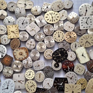 May include: A collection of vintage watch faces in various shapes and sizes, including round, square, and oval. The faces are in shades of cream, gold, and black, with visible hands and numerals. A variety of styles are present, suggesting a collection of watchmaking components.