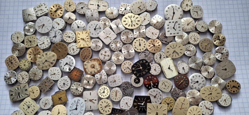 May include: A collection of vintage watch faces in various shapes and sizes, including round, square, and oval. The faces are in shades of cream, gold, and black, with visible hands and numerals. A variety of styles are present, suggesting a collection of watchmaking components.