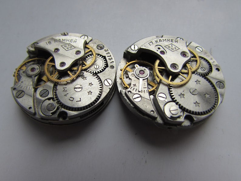 May include: Two silver watch movements with gold gears and screws. The text "15 камней" and "17 камней" is visible on the top of each movement.