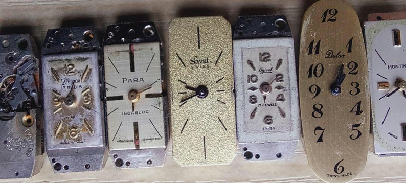 May include: A collection of vintage watch faces, showcasing various designs and styles. The faces include Roman and Arabic numerals, with brands like 'Gregdel', 'Para', and 'Dulux'. The colors are primarily silver, gold, and black, with visible watch mechanisms.