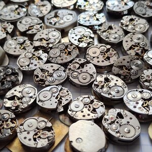 May include: A collection of vintage watch movements, showcasing intricate gears and mechanical components. The silver-toned metal parts are arranged in a scattered pattern, highlighting the detailed craftsmanship of each piece. Ideal for steampunk projects or watch repair.