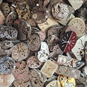 K&ouml;nnte beinhalten: Eine Sammlung von Vintage-Uhrenteilen, darunter Zifferbl&auml;tter, Zahnr&auml;der und Innenmechanismen. Die Zifferbl&auml;tter variieren in Form und Farbe, einige mit r&ouml;mischen Ziffern und andere mit arabischen Ziffern. Die Zahnr&auml;der sind aus Metall und aufwendig gestaltet.