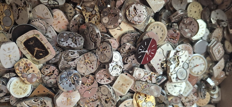 K&ouml;nnte beinhalten: Eine Sammlung von Vintage-Uhrenteilen, darunter Zifferbl&auml;tter, Zahnr&auml;der und Innenmechanismen. Die Zifferbl&auml;tter variieren in Form und Farbe, einige mit r&ouml;mischen Ziffern und andere mit arabischen Ziffern. Die Zahnr&auml;der sind aus Metall und aufwendig gestaltet.