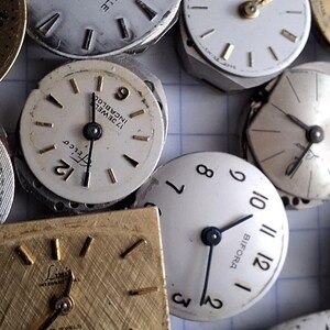 May include: A collection of vintage watch faces, showcasing various designs and brands. The faces are primarily white with black numerals and hands, some with gold accents. The assortment includes round and square shapes, offering a glimpse into watchmaking history.