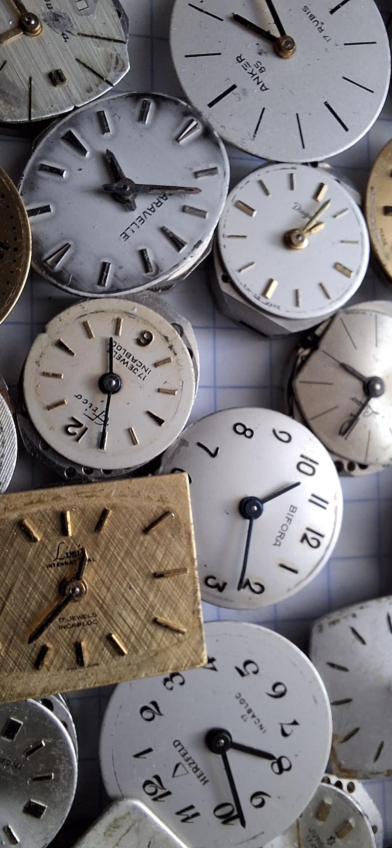 May include: A collection of vintage watch faces, showcasing various designs and brands. The faces are primarily white with black numerals and hands, some with gold accents. The assortment includes round and square shapes, offering a glimpse into watchmaking history.
